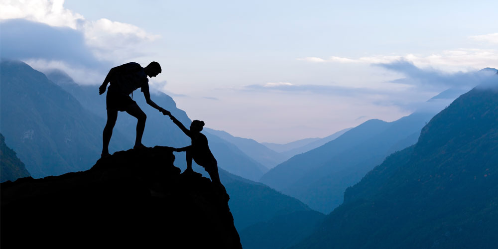 man helping woman climb cliff